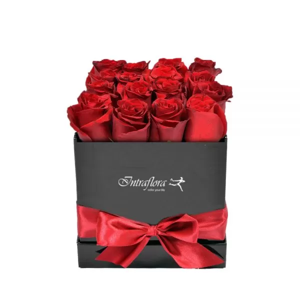 A black square box filled with red roses, decorated with a red ribbon and bow, against a white background. The box also features the "Intraflora" logo.