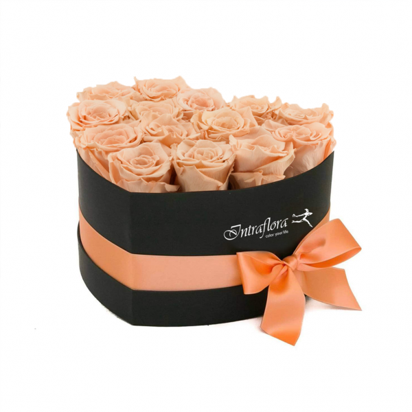 A black, heart-shaped box filled with peach roses, wrapped with a peach ribbon and bow, against a white background. The box also features the "Intraflora" logo.