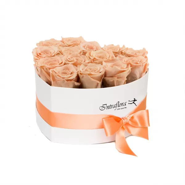 A white, heart-shaped box filled with peach roses, wrapped with a peach ribbon and bow, against a white background. The box also features the "Intraflora" logo.