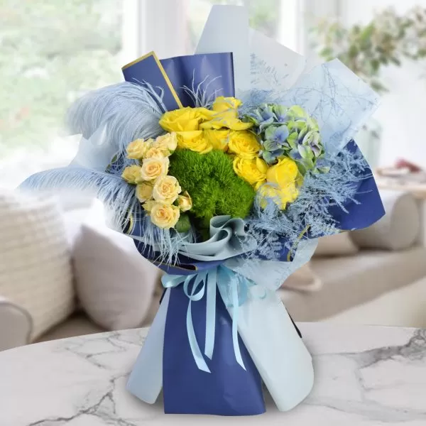 A bouquet of yellow roses, blue hydrangeas, and green dianthus, wrapped in blue and light blue paper and tied with a light blue ribbon, placed on a marble table with a blurred background. The bouquet also features light blue feathers as decorations.
