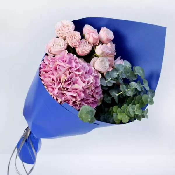A close-up shot of a bouquet featuring small pink roses, a pink hydrangea, and eucalyptus leaves, wrapped in bright blue paper and tied with a gray ribbon.