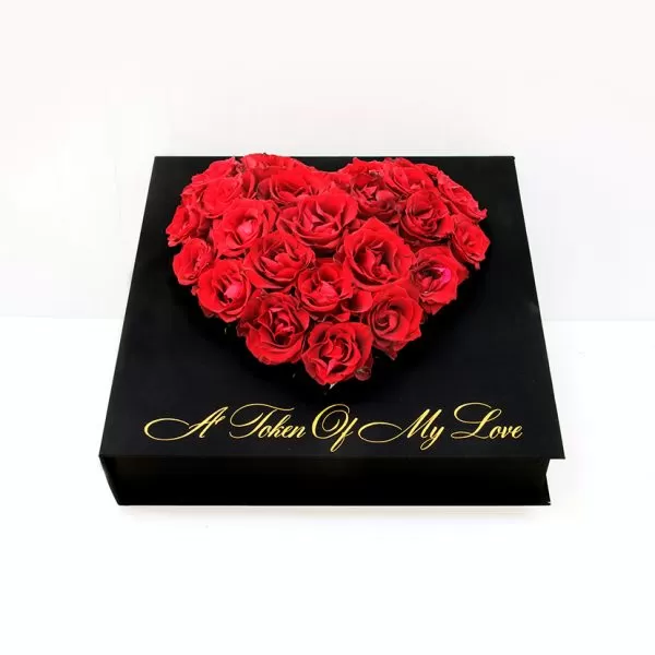 A black square box with a heart-shaped arrangement of red roses on top. The phrase "A Token Of My Love" is written in gold script on the front of the box.