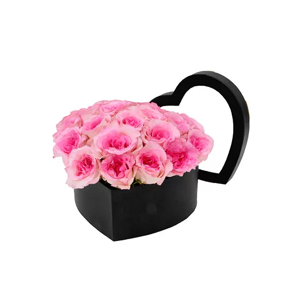 A black, heart-shaped box filled with pink roses, viewed from an angle, showcasing the texture and shape of the box.