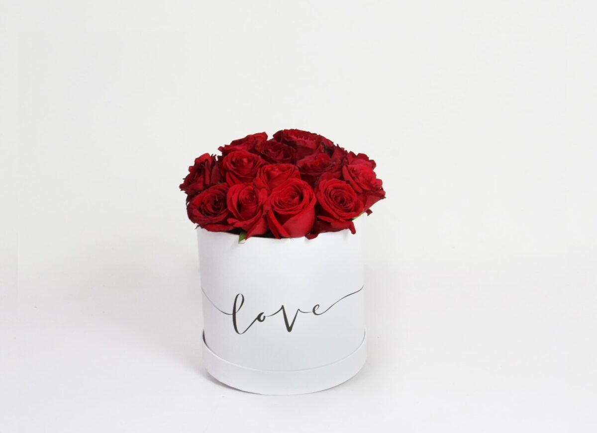 A white, cylindrical flower box filled with dark red roses, with the word "love" written in black script on the side, against a light background.