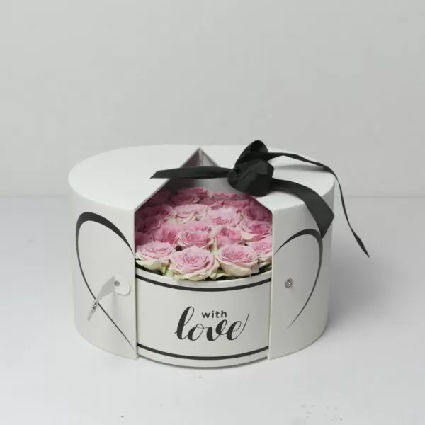 A white, round flower box with a triangular cutout in the lid, revealing pink roses inside. The box is decorated with a black bow, two outlined hearts on the sides, and the phrase "with love" written on the front.