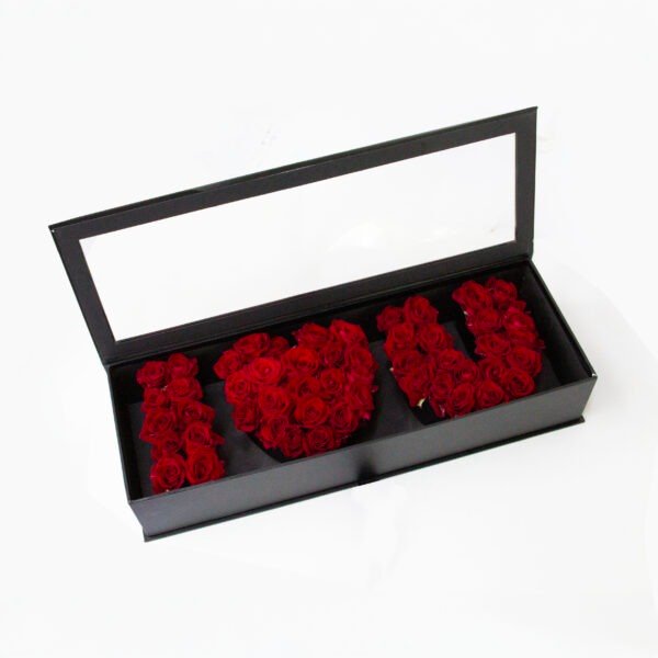 A black rectangular box with a transparent lid, containing dark red roses arranged to spell out "I [heart] U".