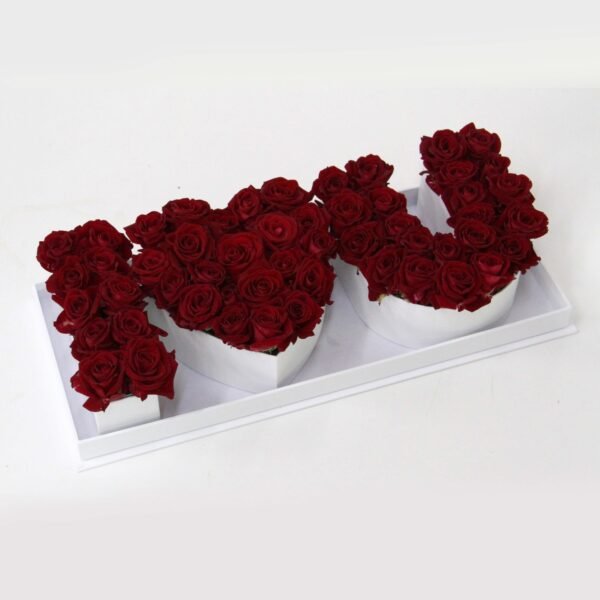 A white rectangular tray containing three white heart-shaped boxes, each filled with dark red roses, spelling out "I [heart] U".