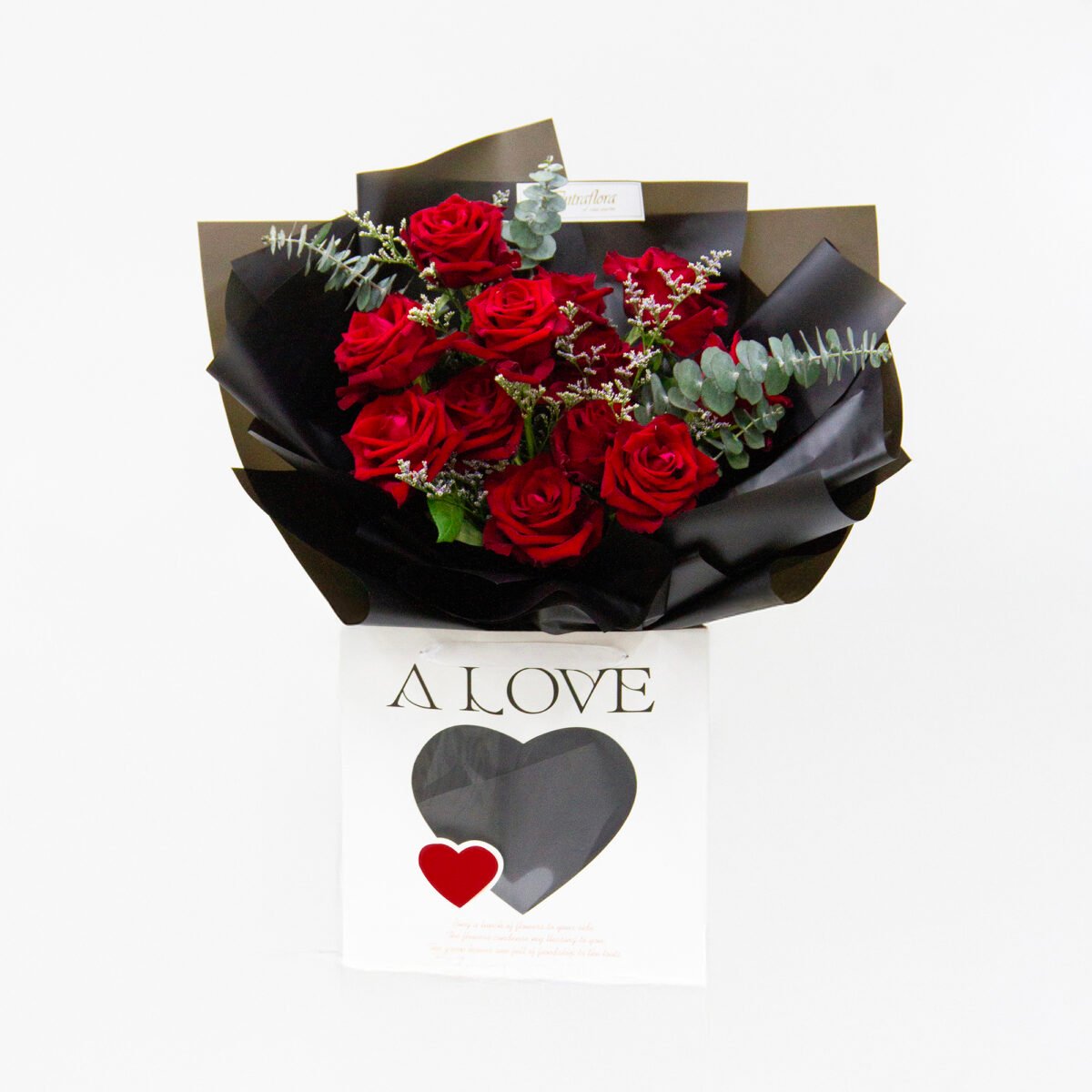 Elegant bouquet with 12 Ever Red roses, 2 purple limonium caspia, and 5 eucalyptus cinerea, wrapped in black with a black ribbon, presented in a white bag.