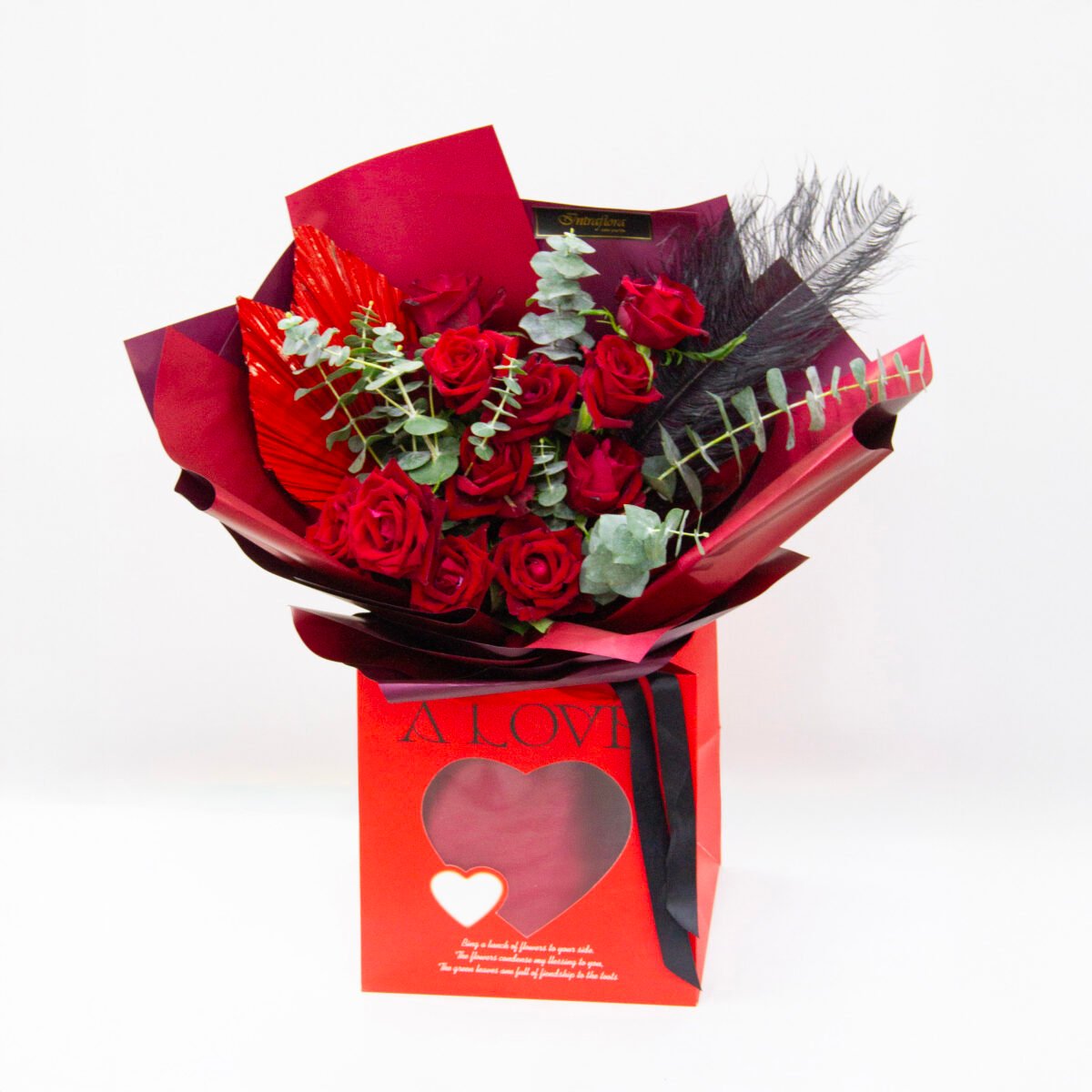 Elegant bouquet with Ever Red roses, eucalyptus cinerea, black feathers, wrapped in black with a black ribbon, presented in a red bag
