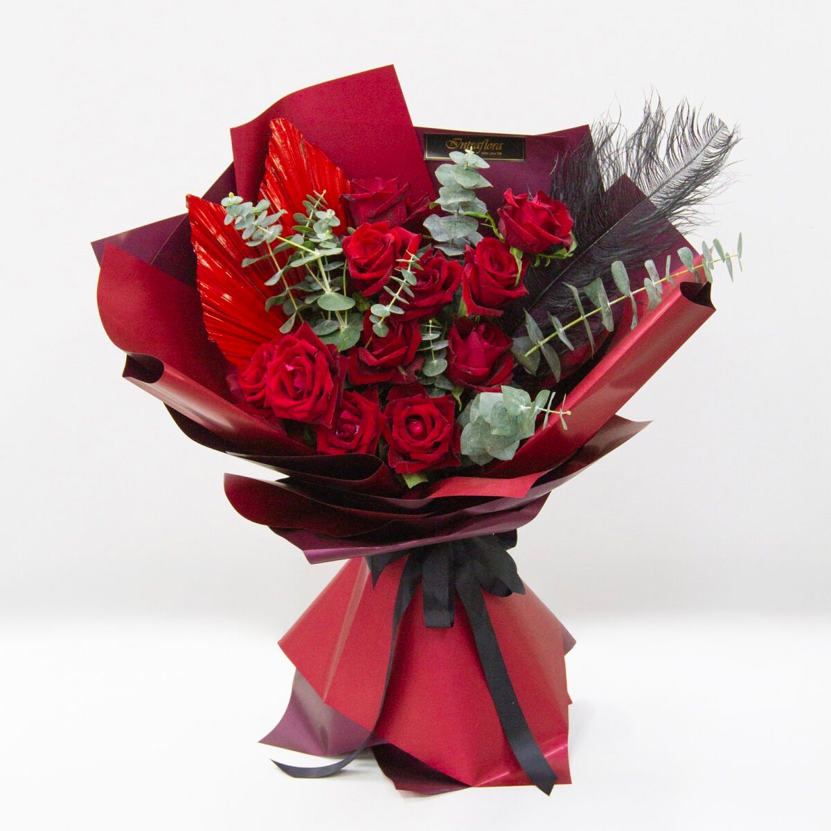 Red Aura bouquet with 12 Ever Red roses, eucalyptus cinerea, black feathers, wrapped in red with a black ribbon."