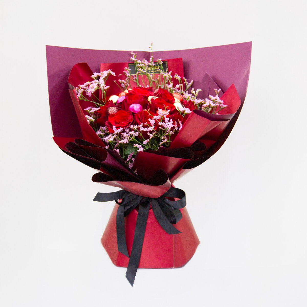 Elegant bouquet with 12 premium red roses, 5 pink limonium caspia, wrapped in red with a black ribbon, paired with mini heart-shaped chocolates.